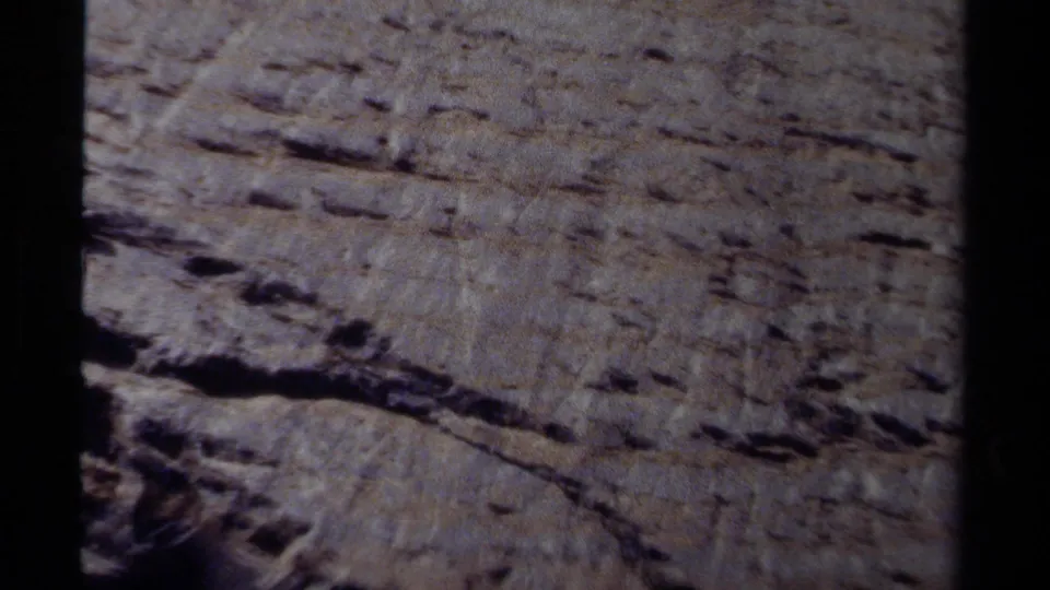 1979 British Columbia 8mm frame showing a close view of a sheer, layered rock wall in daylight.