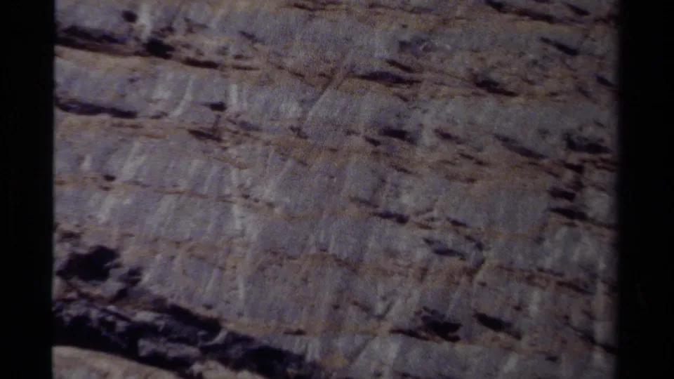 8mm frame from British Columbia showing a steep rock wall with layered ledges and shadowed recesses.