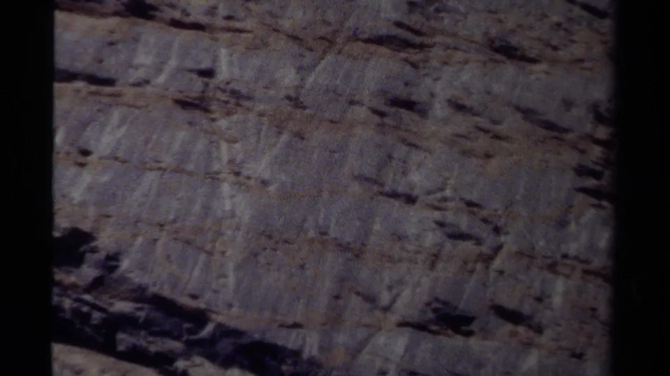 Home-movie frame of a British Columbia rock wall, showing rough strata and faded 8mm color.