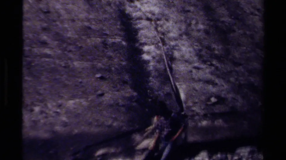 1979 British Columbia 8mm frame with a small walking figure near the base of a sheer, shadowed rock wall.