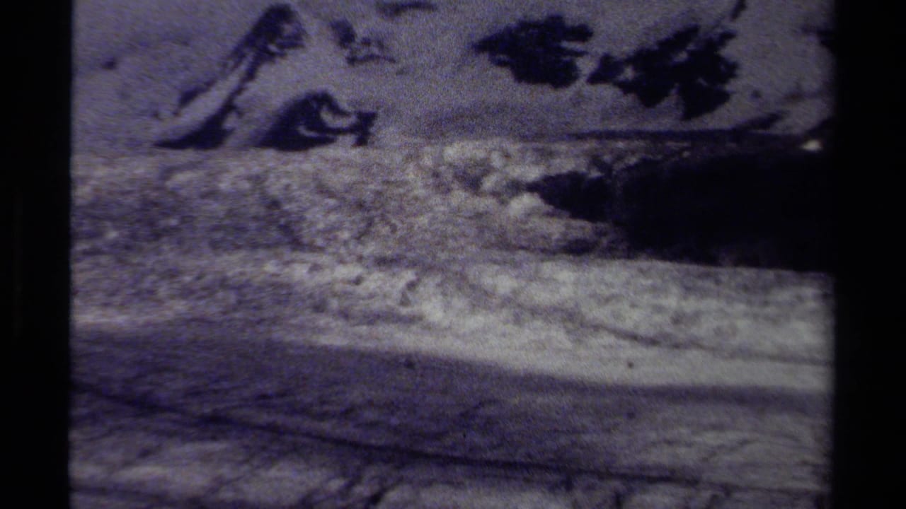 Faded 8mm view of a snowy British Columbia mountain or glacier area with dark exposed rock and visible film-frame borders.
