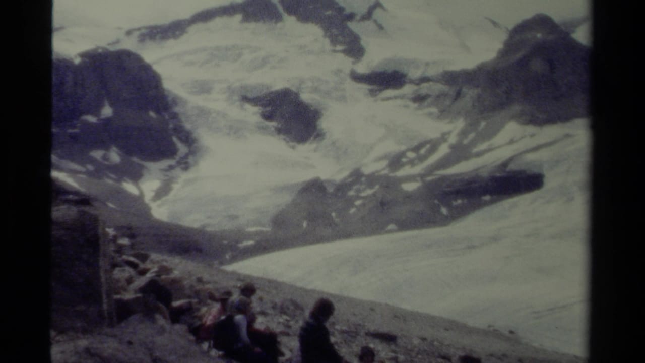 1979 British Columbia 8mm frame showing hikers seated on scree beneath broad snowy alpine slopes.