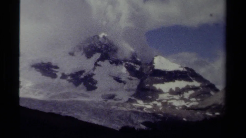 1979 British Columbia 8mm frame looking across snowy peaks, dark rock bands, and clouds.
