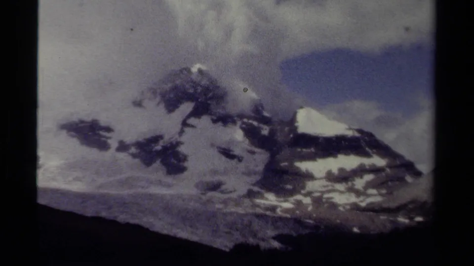 1979 British Columbia home-movie frame of snowy mountain peaks with clouds and a patch of blue sky.