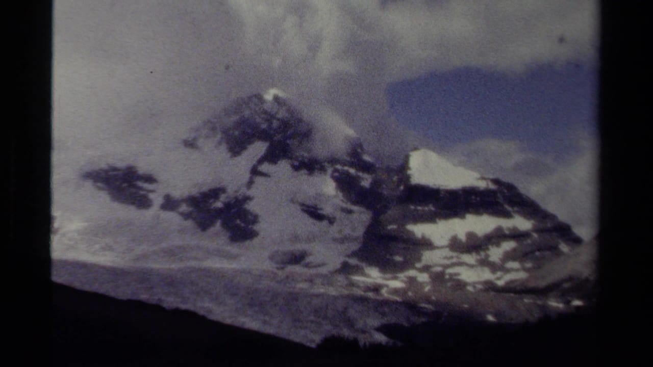 Snow-capped mountain peaks under a cloudy sky with dark film borders.