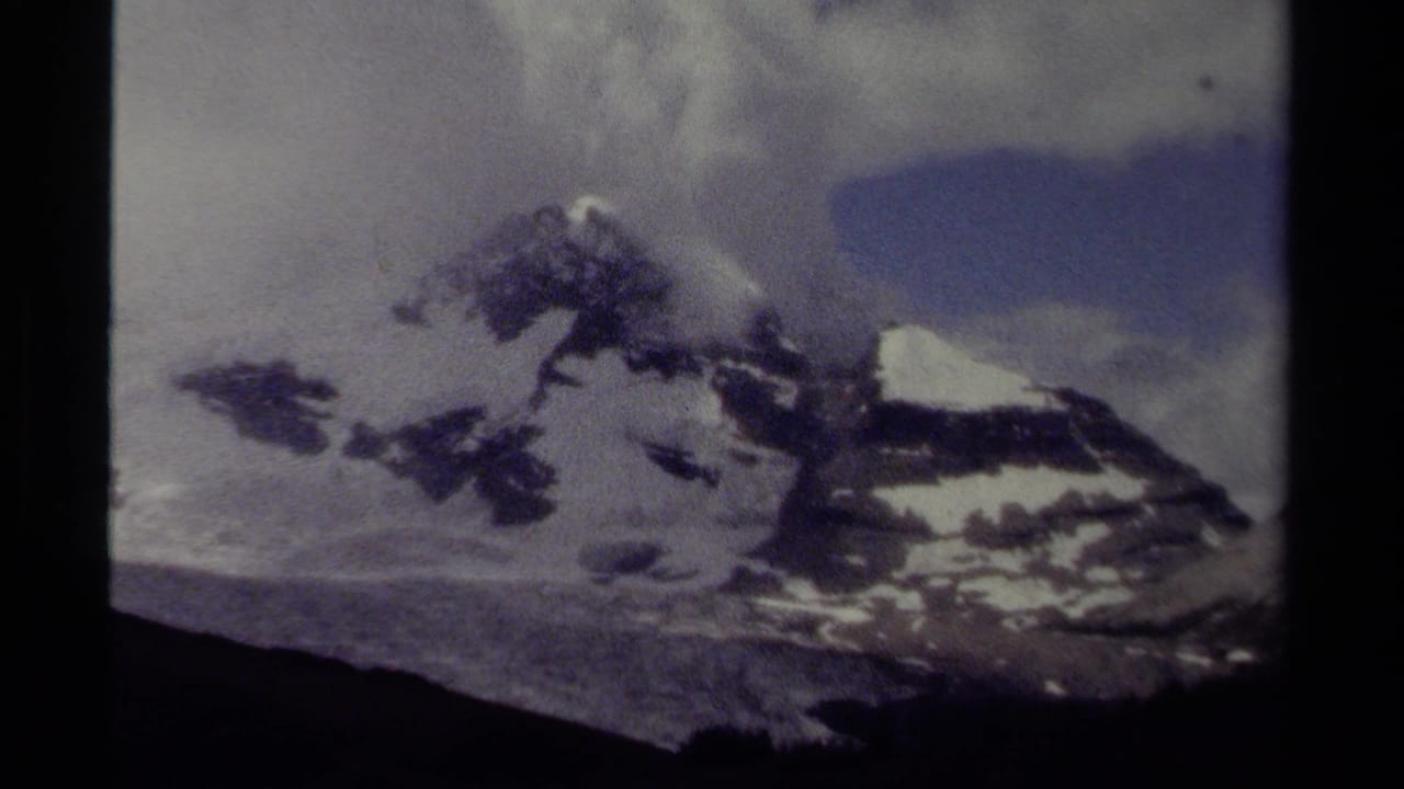 Distant snowy mountain range beneath clouds with dark vertical film edge.