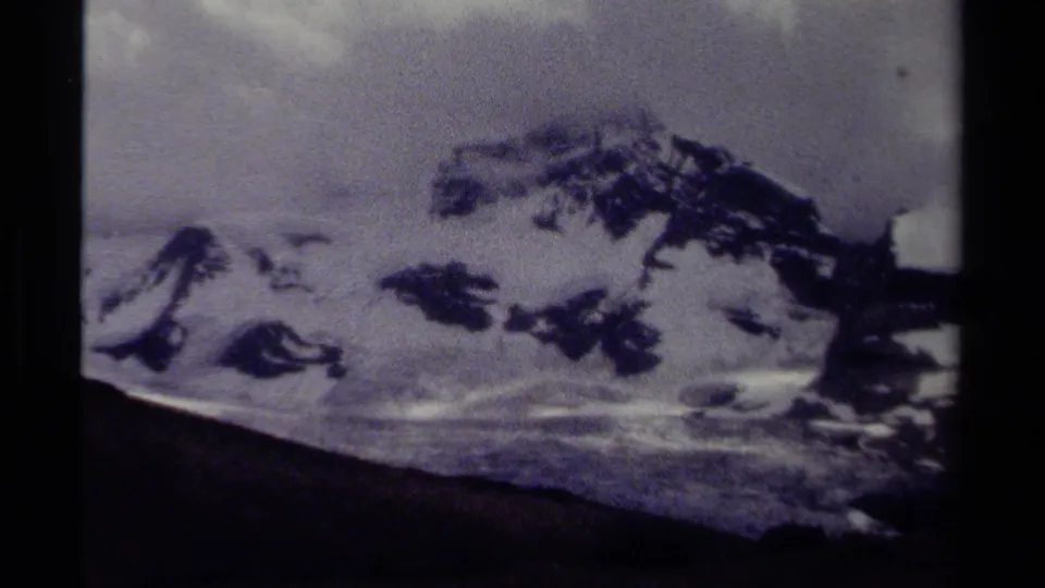 Grainy 8mm view of British Columbia mountain ridges with snow patches and a muted clouded sky, dated 1979 by metadata.