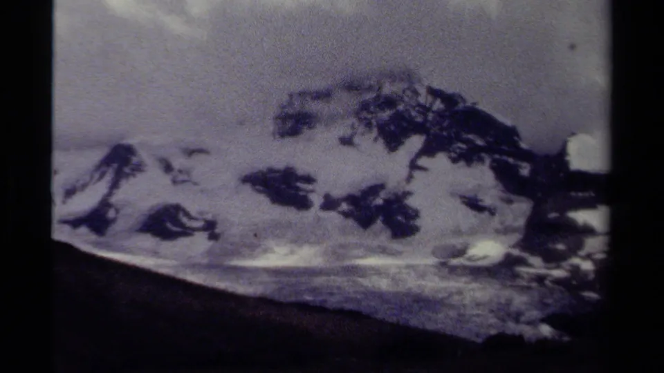 1979 8mm view of a snow-covered mountain ridge in British Columbia, with dark slopes and cloudy sky.