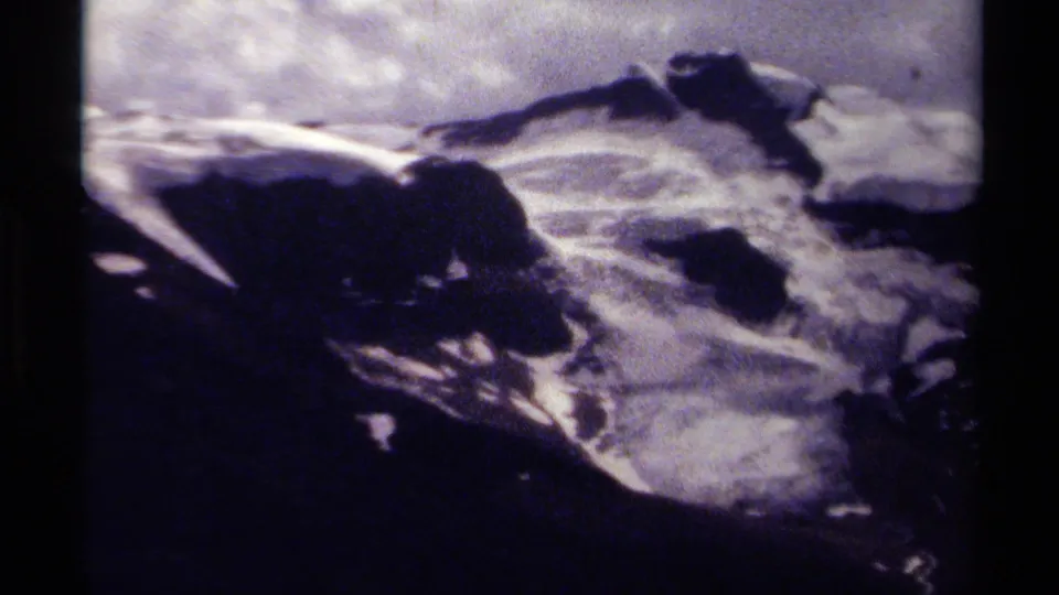 British Columbia 8mm frame from 1979 showing distant snowy peaks, dark foreground slopes, and cloudy light.