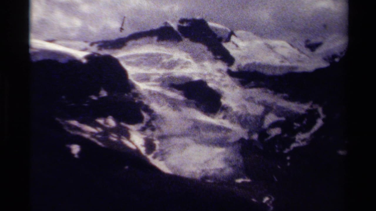1979 8mm frame showing a rugged British Columbia alpine slope with snow, dark ridgeline shadows, cloudy sky, and visible film grain.