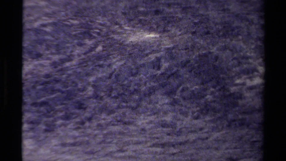 1979 British Columbia 8mm frame showing a dark, grainy rocky mountain surface with pale mineral streaks and shadowed cracks.