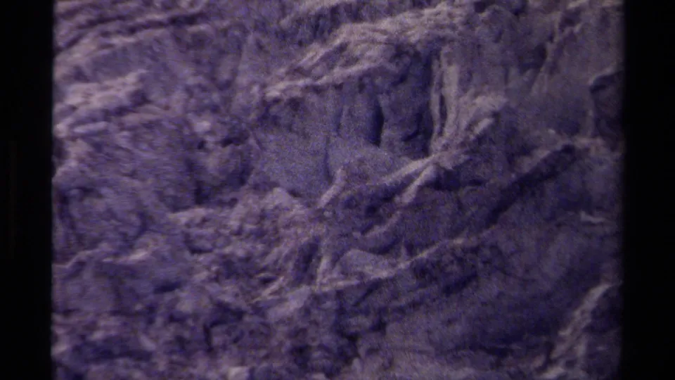 1979 British Columbia 8mm frame of a rugged mountain rock face with pale streaks, broken surfaces, and shadowed recesses.