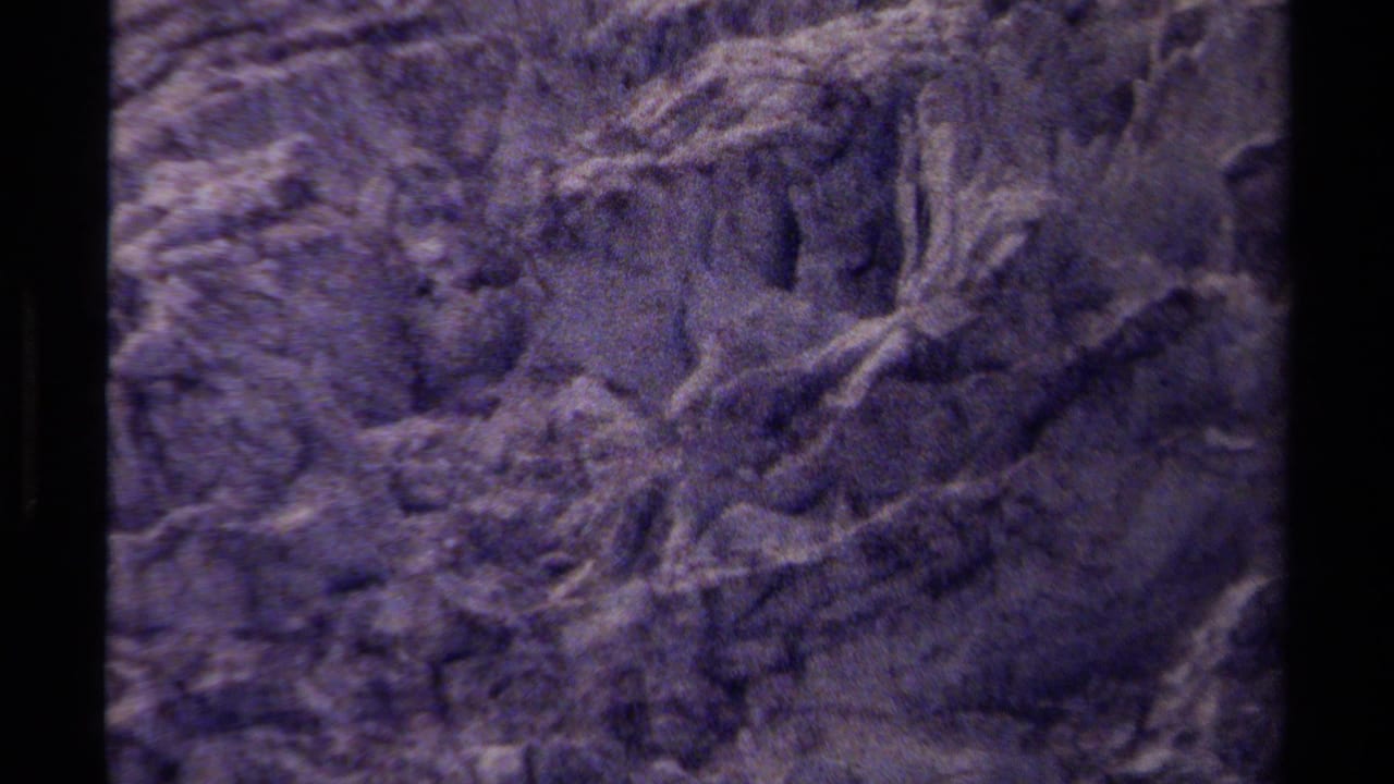 Close view of a rough rock face in grainy purple-blue 8mm footage.