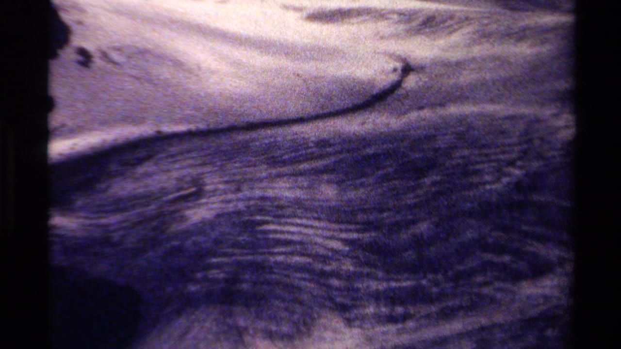 1979 British Columbia 8mm home-movie frame showing rippling river water moving across shallow rocks with faded color and dark borders.