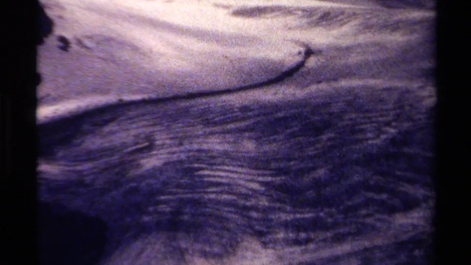 1979 British Columbia 8mm home-movie frame showing rippling river water moving across shallow rocks with faded color and dark borders.