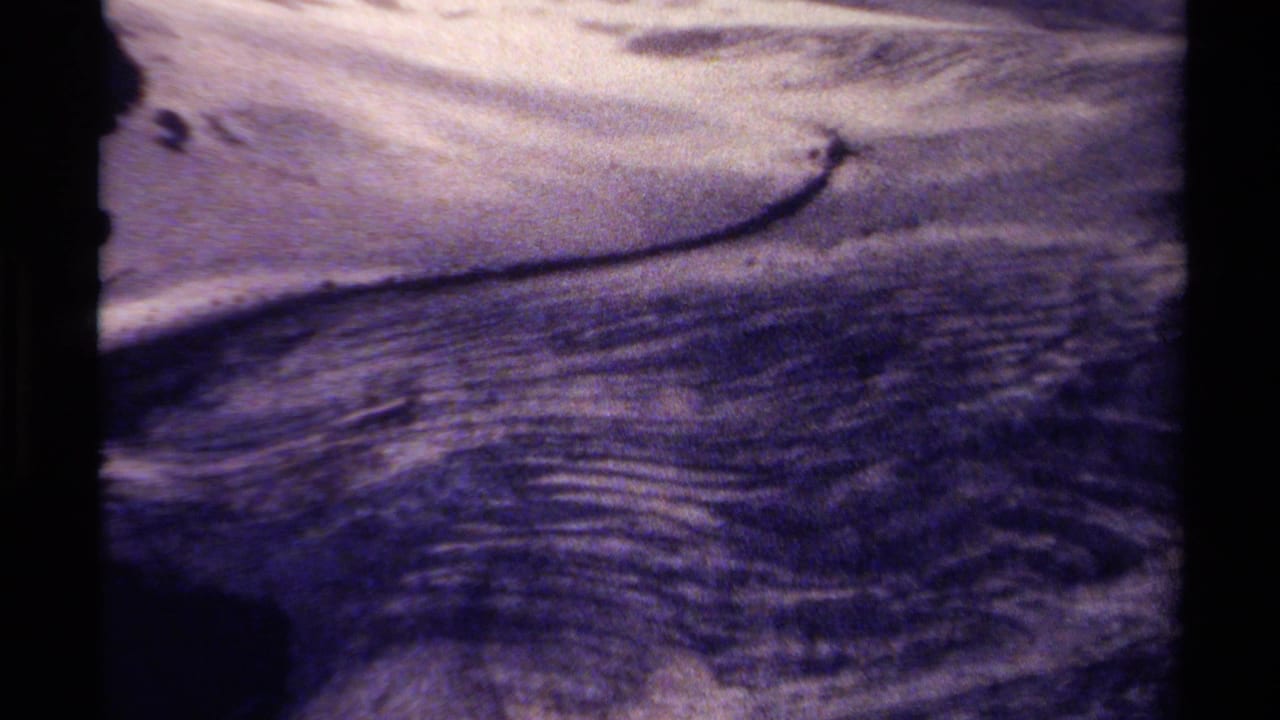 Faded 8mm frame from British Columbia showing moving stream water over rocks, with a dark contact-sheet divider at the side.