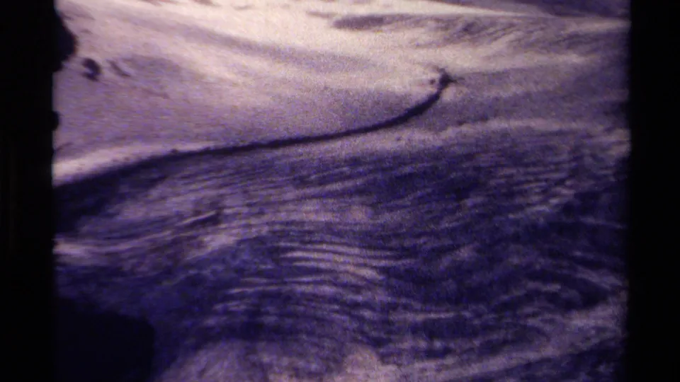 Faded 8mm frame from British Columbia showing moving stream water over rocks, with a dark contact-sheet divider at the side.
