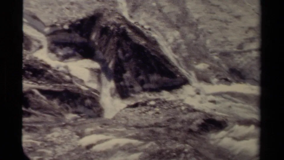 British Columbia 8mm frame showing white water and small cascades moving around larger rocks in a close, grainy river view.