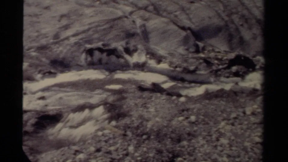 1979 British Columbia home-movie frame of a rough stream bed with whitewater and uneven rocky banks.