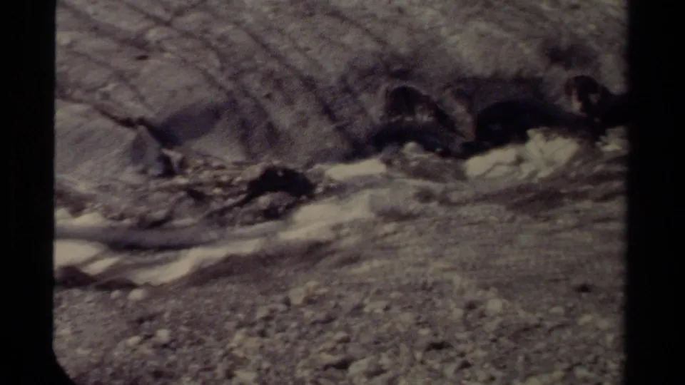 1979 British Columbia 8mm frame showing a shallow, turbulent stream moving past dark rocks and gravel.