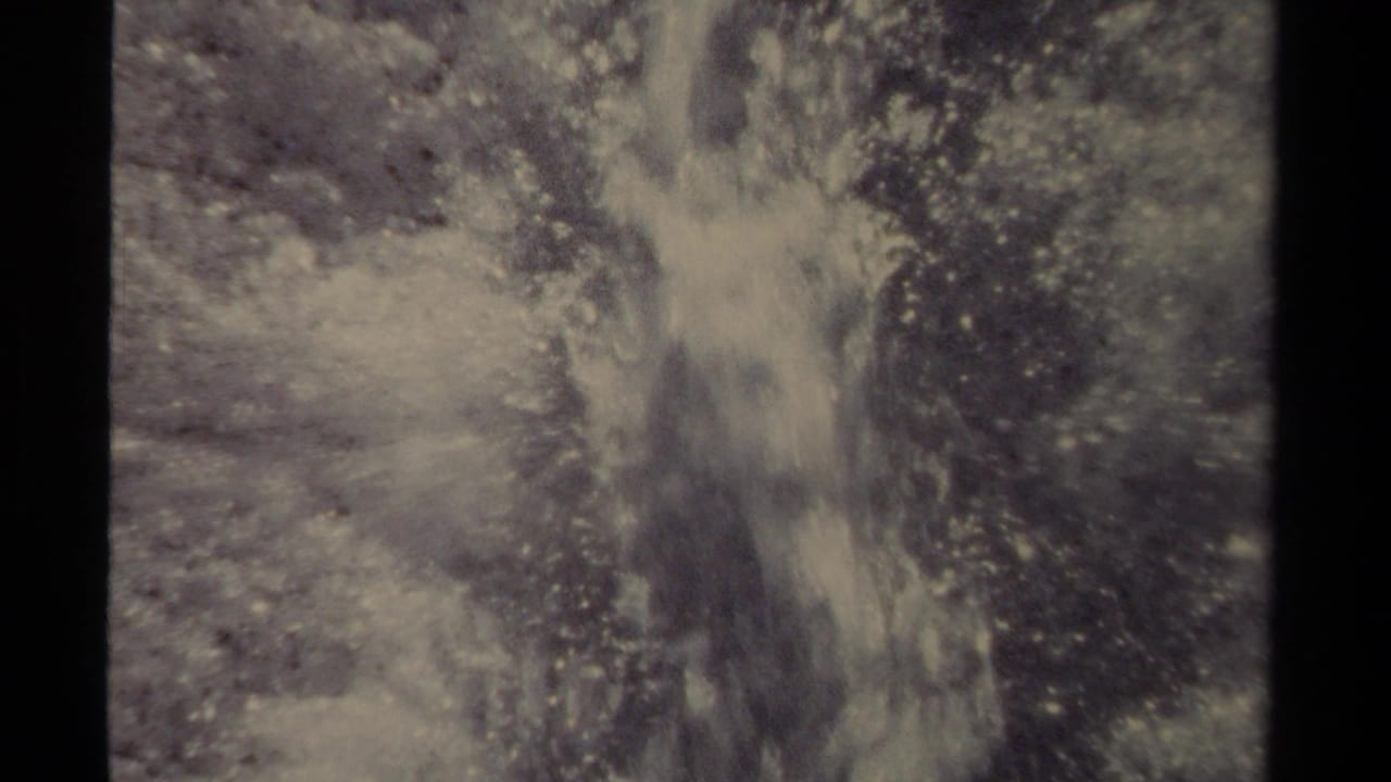 Narrow water stream splashing through ice on frozen ground.