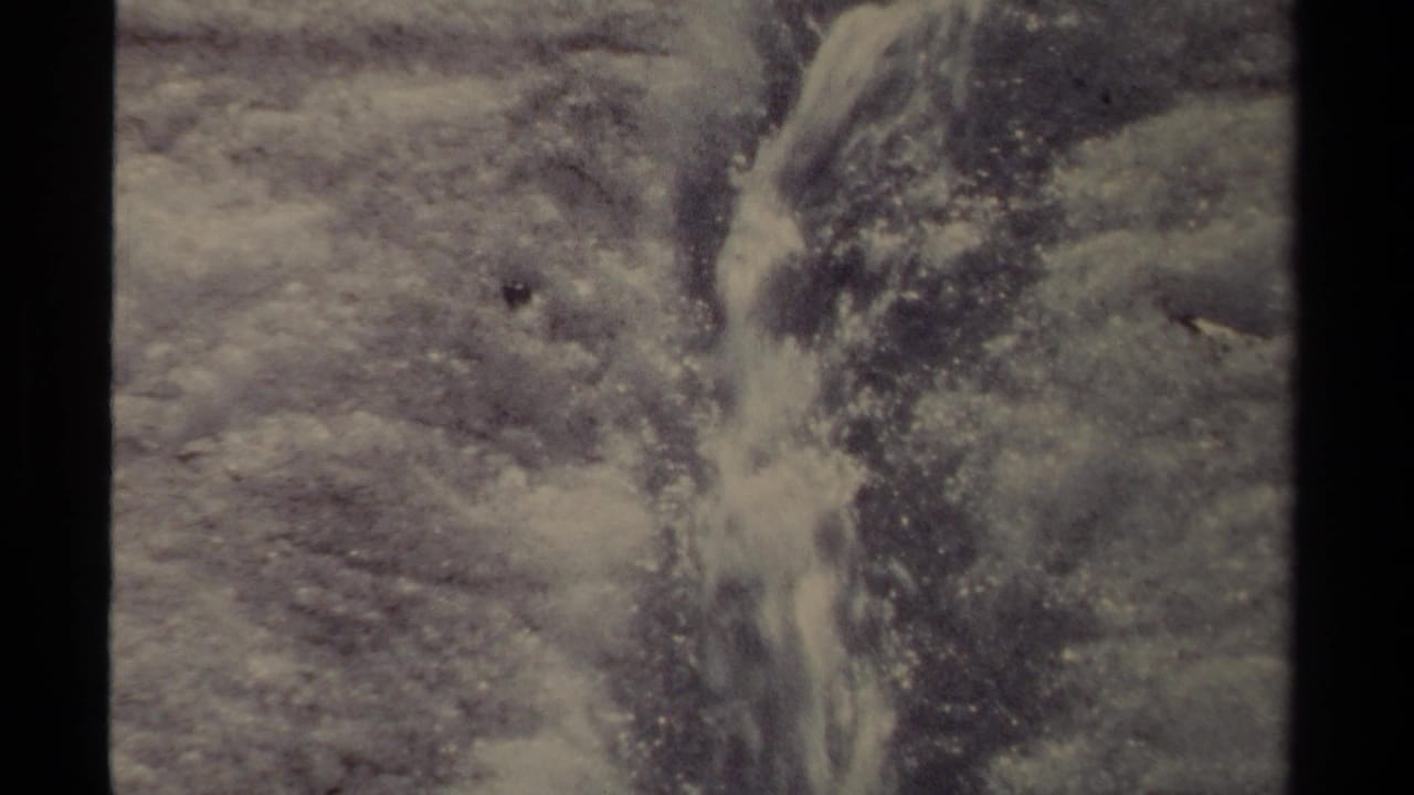 Water runs down a narrow channel in ice, framed by film borders.