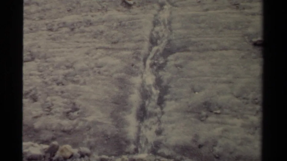 1979 British Columbia frame showing a thin stream descending through an ice channel on a frozen hillside surface.