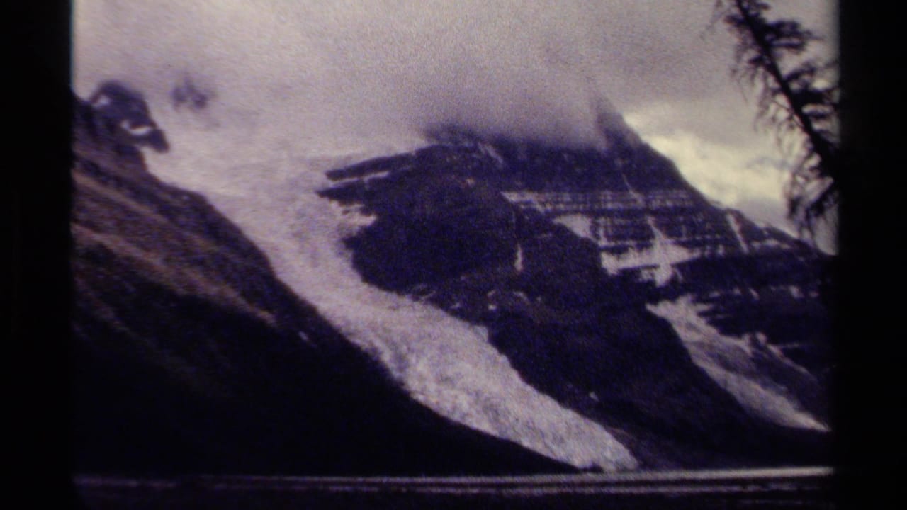 1979 British Columbia 8mm frame showing a foggy snow-covered mountain with dark rocky slopes and foreground tree silhouettes.