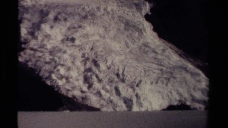 1979 British Columbia 8mm frame showing a rough rock formation viewed from near a road, with heavy grain and dark frame edges.