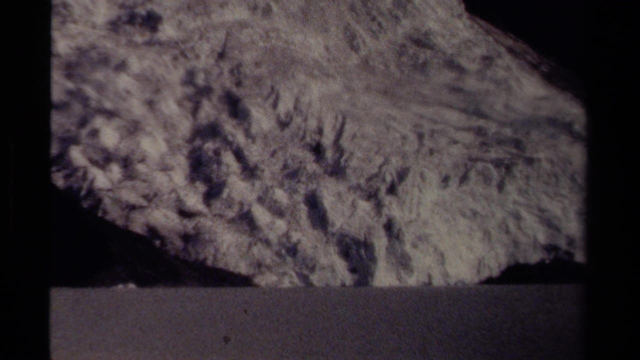 Textured rock face with a dark horizontal foreground band and black film borders.