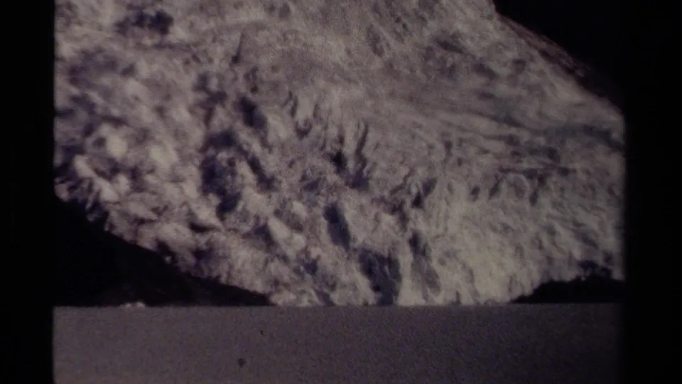 A grainy 8mm view of a massive roadside rock surface in British Columbia, Canada, with no people or signage visible.