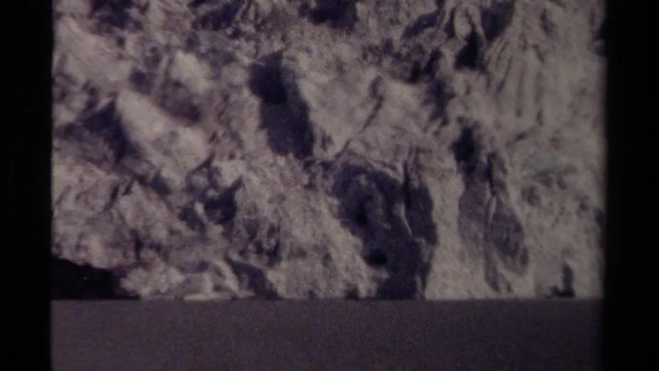 Close 8mm view of icy rock formations in British Columbia, with irregular pale surfaces, dark crevices, and a shadowed lower band.