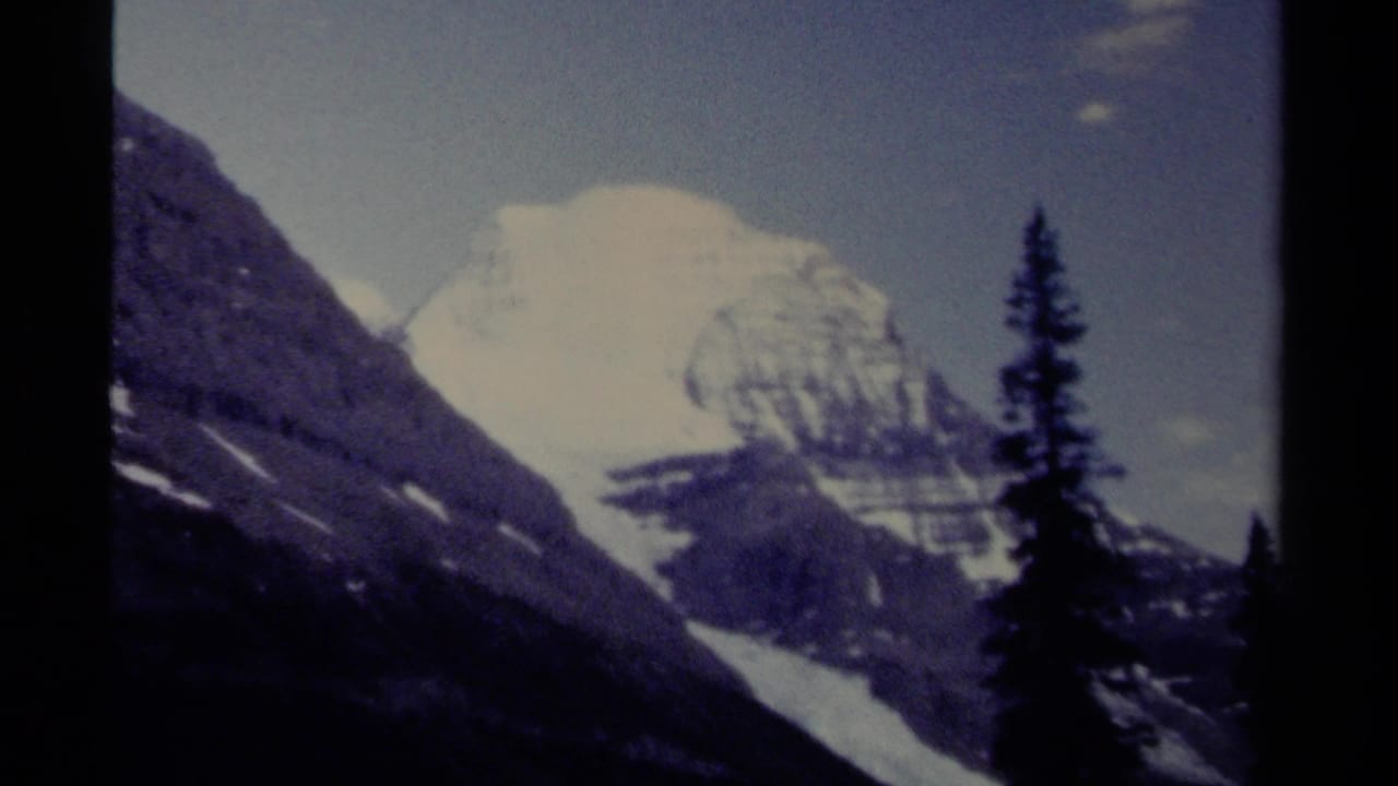 Snow-capped mountain seen beyond dark slopes and evergreen silhouettes.