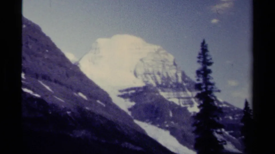 Vintage 8mm view of a British Columbia alpine peak partly softened by mist, with a tall evergreen and dark ridge in the foreground.