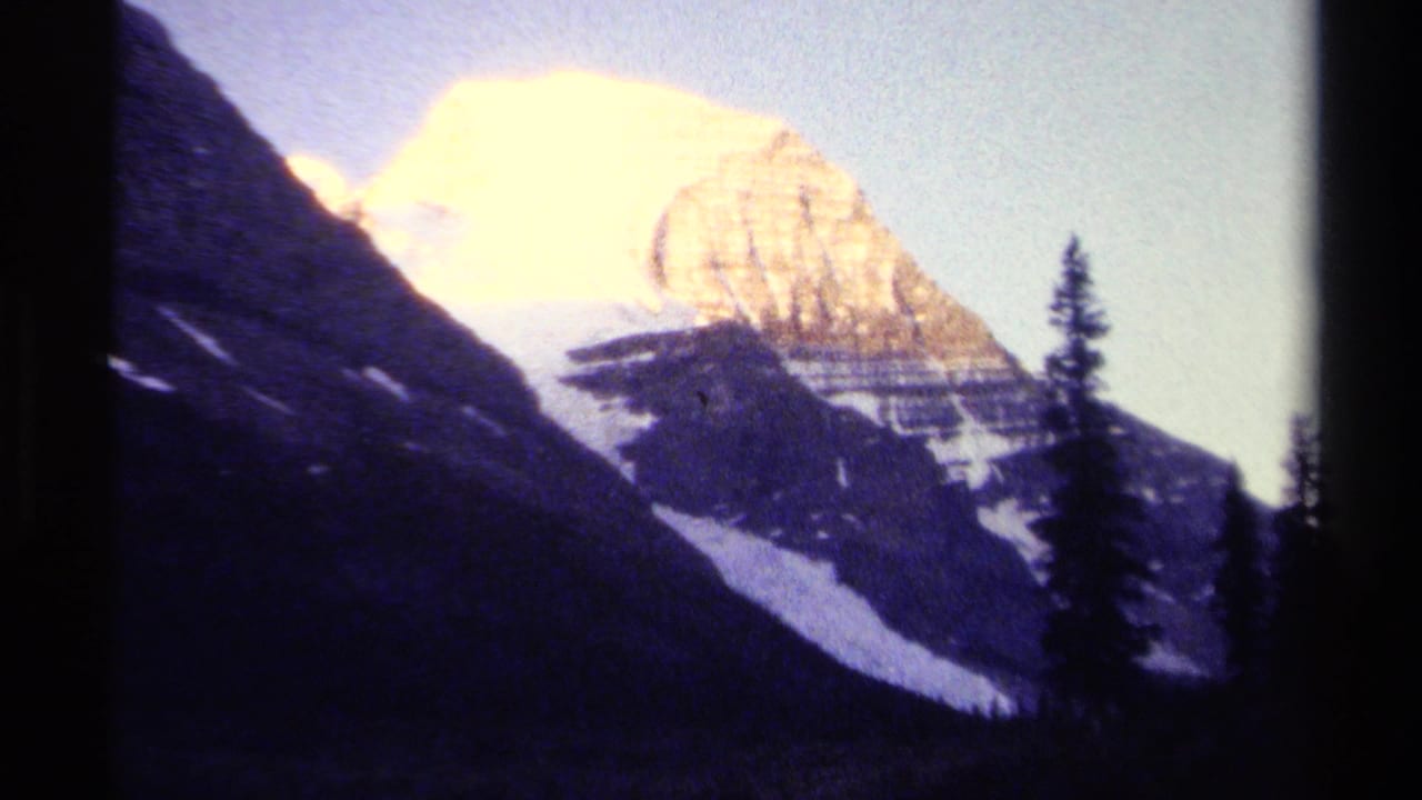 Snowy mountain peak behind dark slopes and evergreen silhouettes.