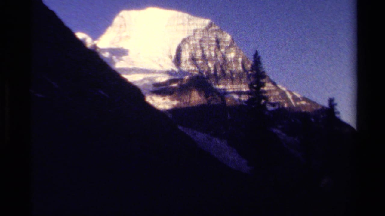 1979 British Columbia 8mm frame showing a bright snowy mountain peak beyond dark pine-covered slopes.