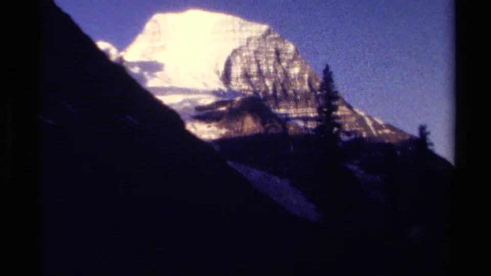 1979 British Columbia 8mm frame showing a bright snowy mountain peak beyond dark pine-covered slopes.