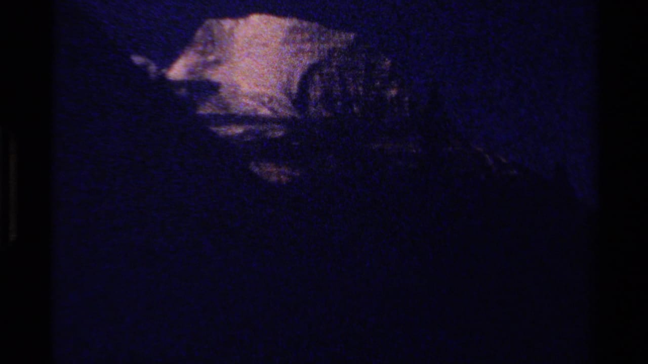 Underexposed 1979 British Columbia 8mm frame with a faint snowy mountain form and heavy blue grain.