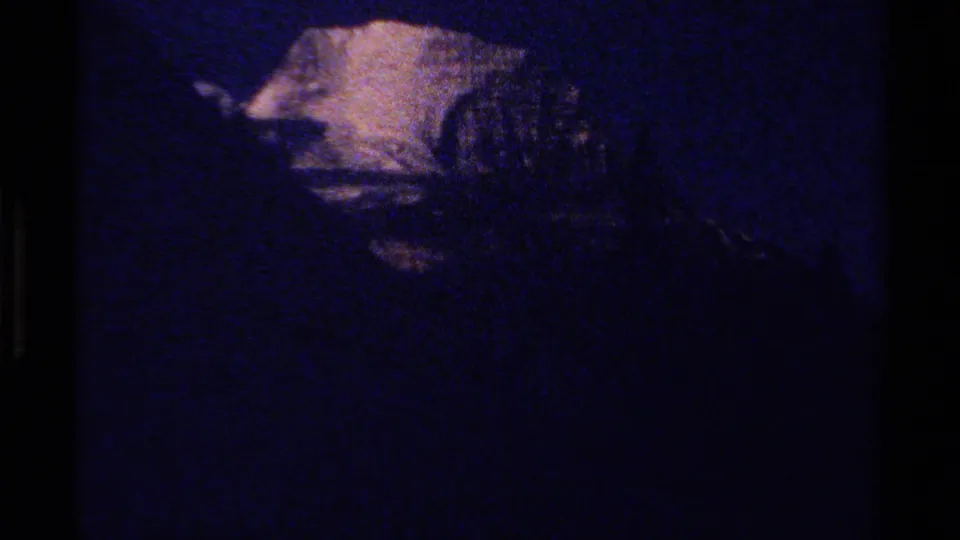 Underexposed 1979 British Columbia 8mm frame with a faint snowy mountain form and heavy blue grain.