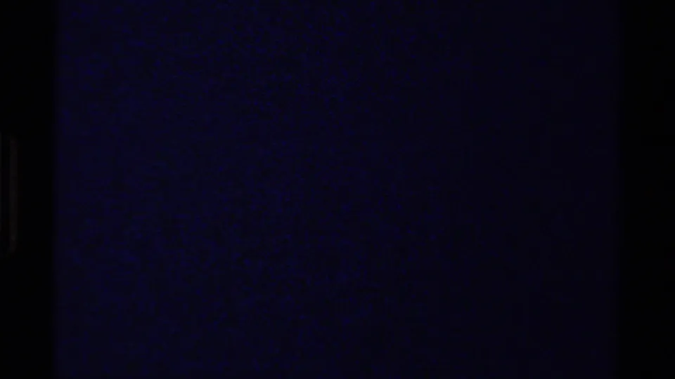 Brief underexposed 8mm frame from the British Columbia mountain clip, dominated by dark blue grain and shadow.