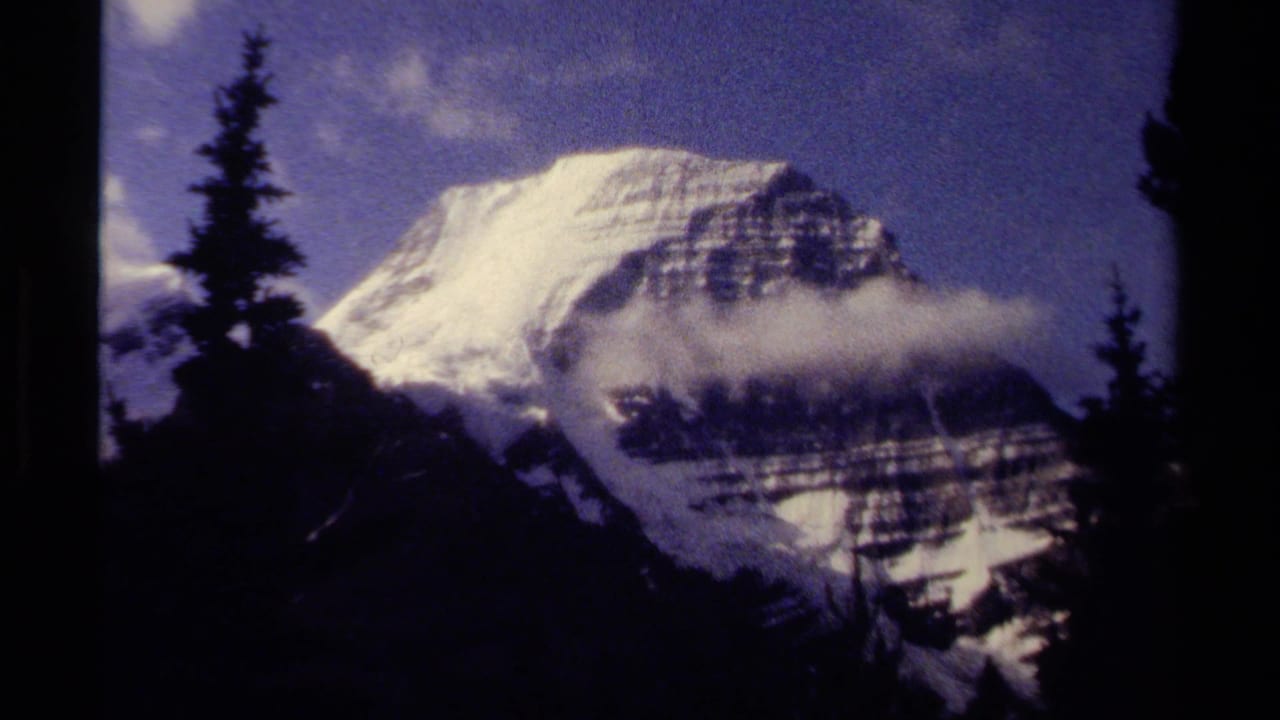 1979 British Columbia 8mm frame showing a snow-capped peak behind low cloud and silhouetted conifers.