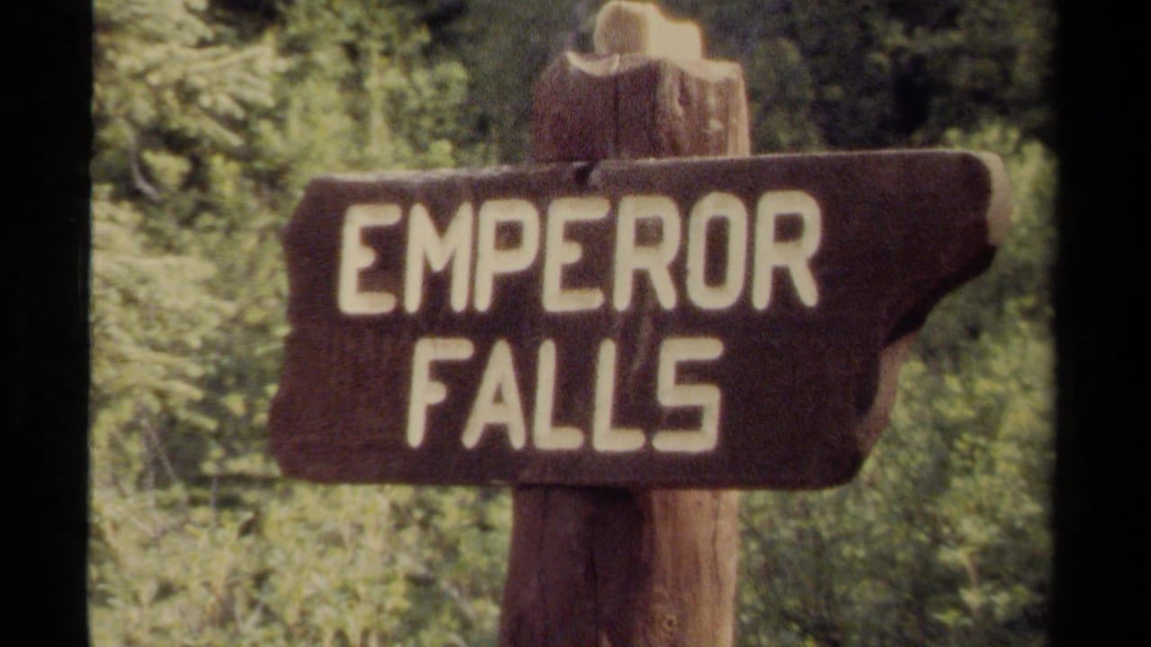 Visitor-shot 8mm view of the Emperor Falls trail sign, with soft focus and saturated green foliage behind it.