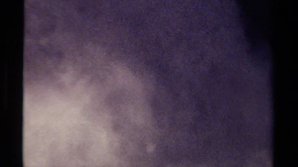 Soft abstract 8mm frame with a pale exposure bloom, dark purple-gray field, and visible black film edge.