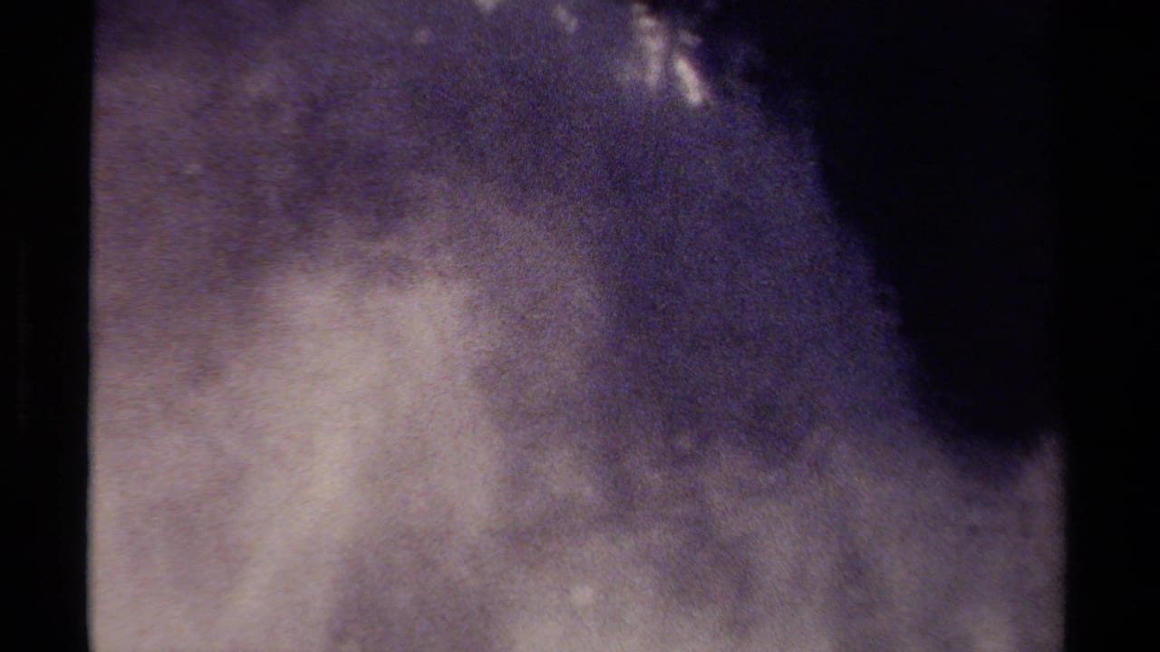 Dark-framed view of a misty waterfall with spray rising against a shadowed background.