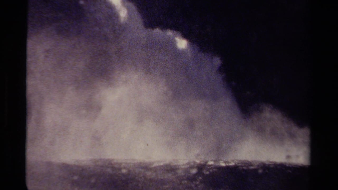 Wide view of white waterfall spray below a dark overhang or shadow.