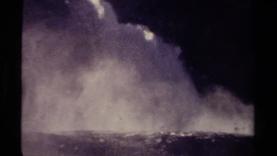 Vintage 8mm view in British Columbia showing waterfall mist spread across the lower frame beneath a dark rocky shadow.