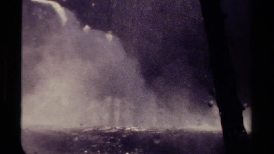 Tight 8mm home-movie frame from British Columbia showing a waterfall edge and pale mist under dark, grainy exposure.