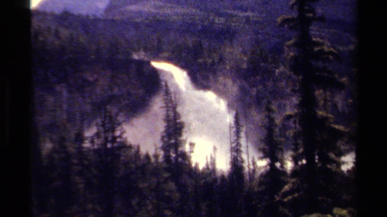 British Columbia mountain waterfall appears beyond evergreen silhouettes in grainy 1979 8mm home-movie footage.