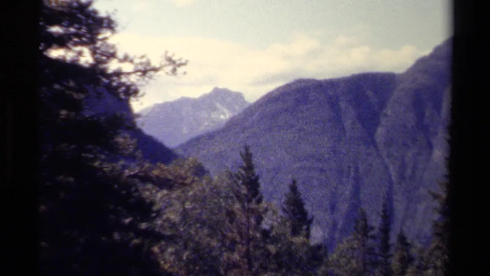 1979 British Columbia 8mm view of layered mountain ridges, treetops, and a pale cloudy sky.