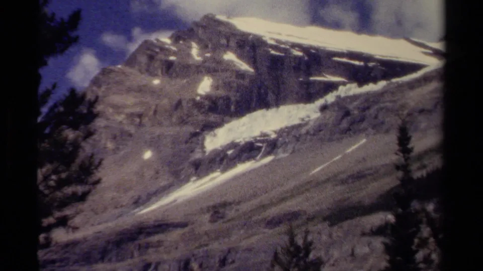 1979 8mm mountain view in British Columbia showing bright snow bands across a rocky peak with trees at the frame edges.
